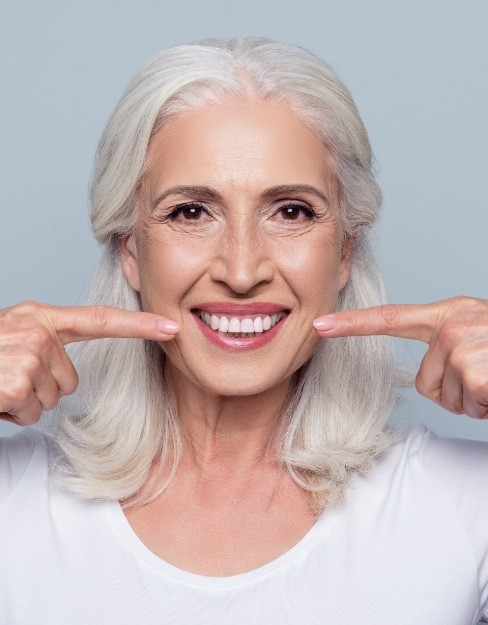 Smiling woman with dentures pointing to her smile