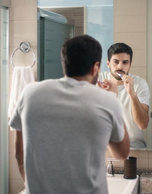Man brushing teeth to maintain dental implants