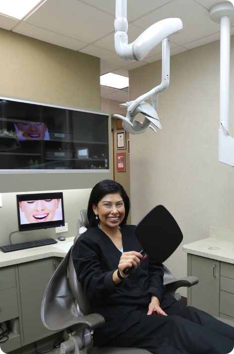 Woman beaming and holding mirror in Houston dental chair