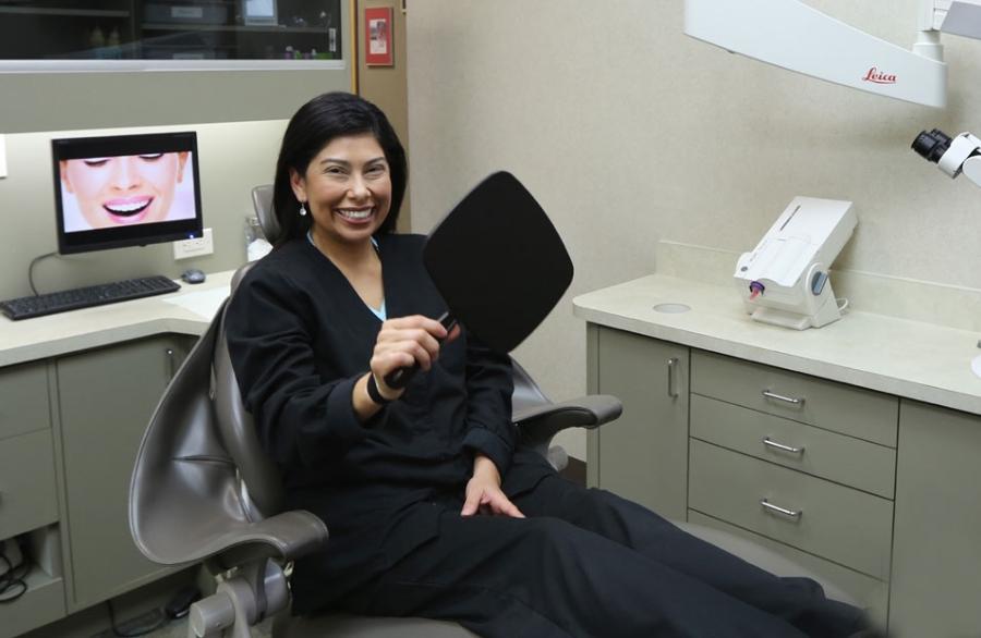 Woman beaming and holding mirror in Houston dental chair