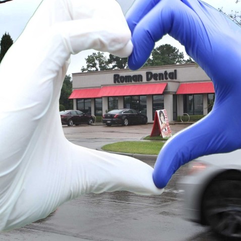 Two gloved hands making a heart shape outside of Roman Dental office in Houston