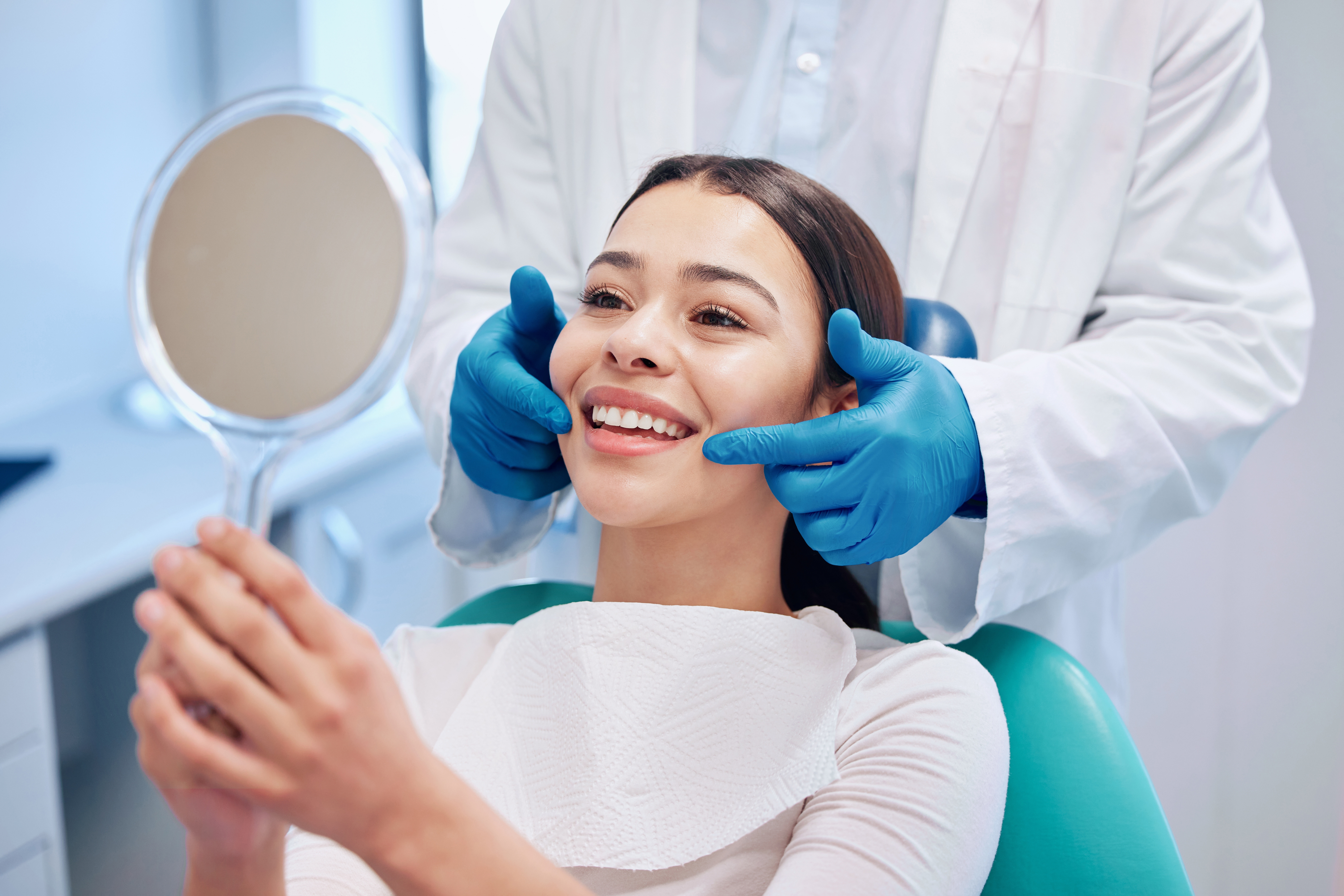 Woman smiling into a mirror after a dental cleaning in Houston, TX