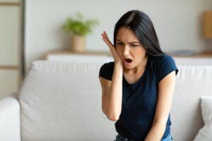 Young woman holding her jaw in pain due to an urgent dental emergency