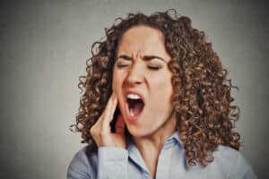 Woman clutching her jaw and back molars in wisdom tooth pain, in need of an extraction