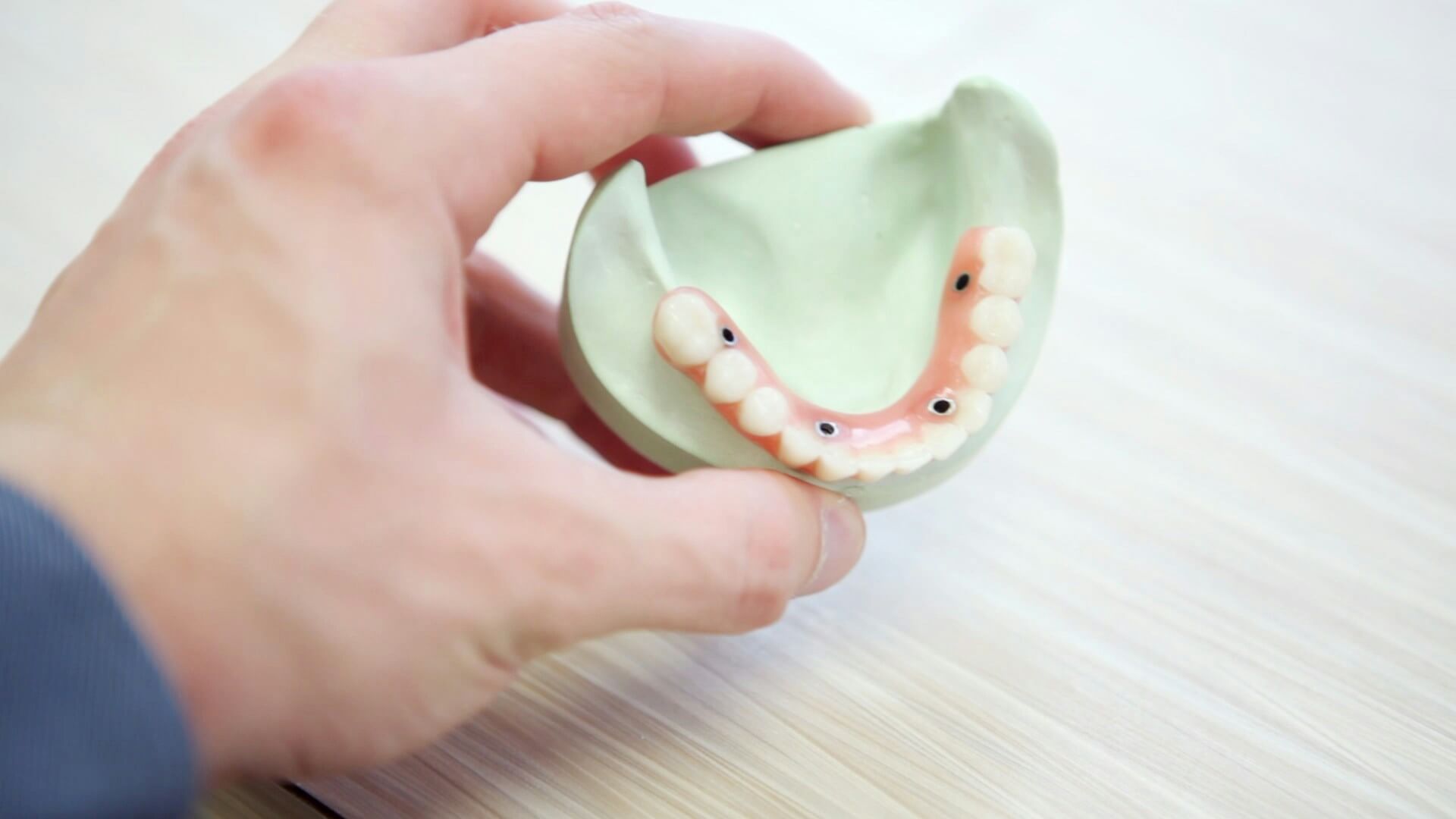 person holding a model of a dental bridge secured by dental implants